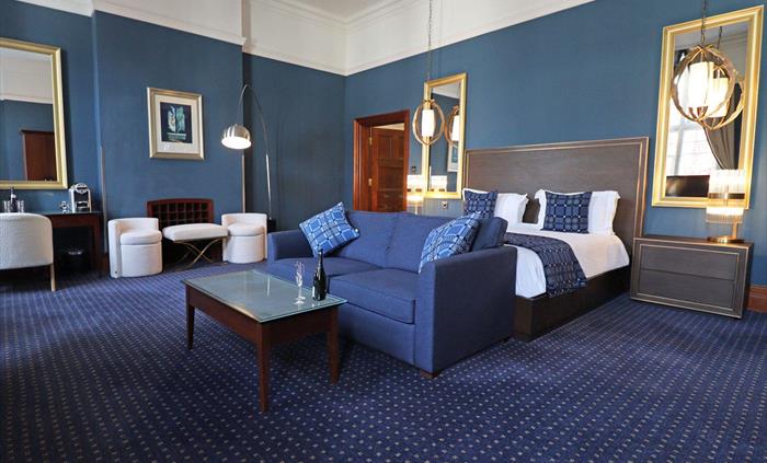 The Henry Belle Suite boasts a stylish Kingside bed, large sofa with coffee table, a desk and comfy chair, and two further comfy chairs